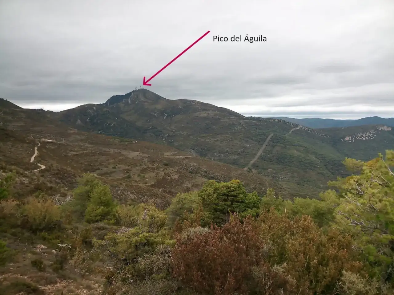 Un sendero serpentea hacia el **Pico del &Aacute;guila**, coronado por antenas, bajo un cielo nublado.
