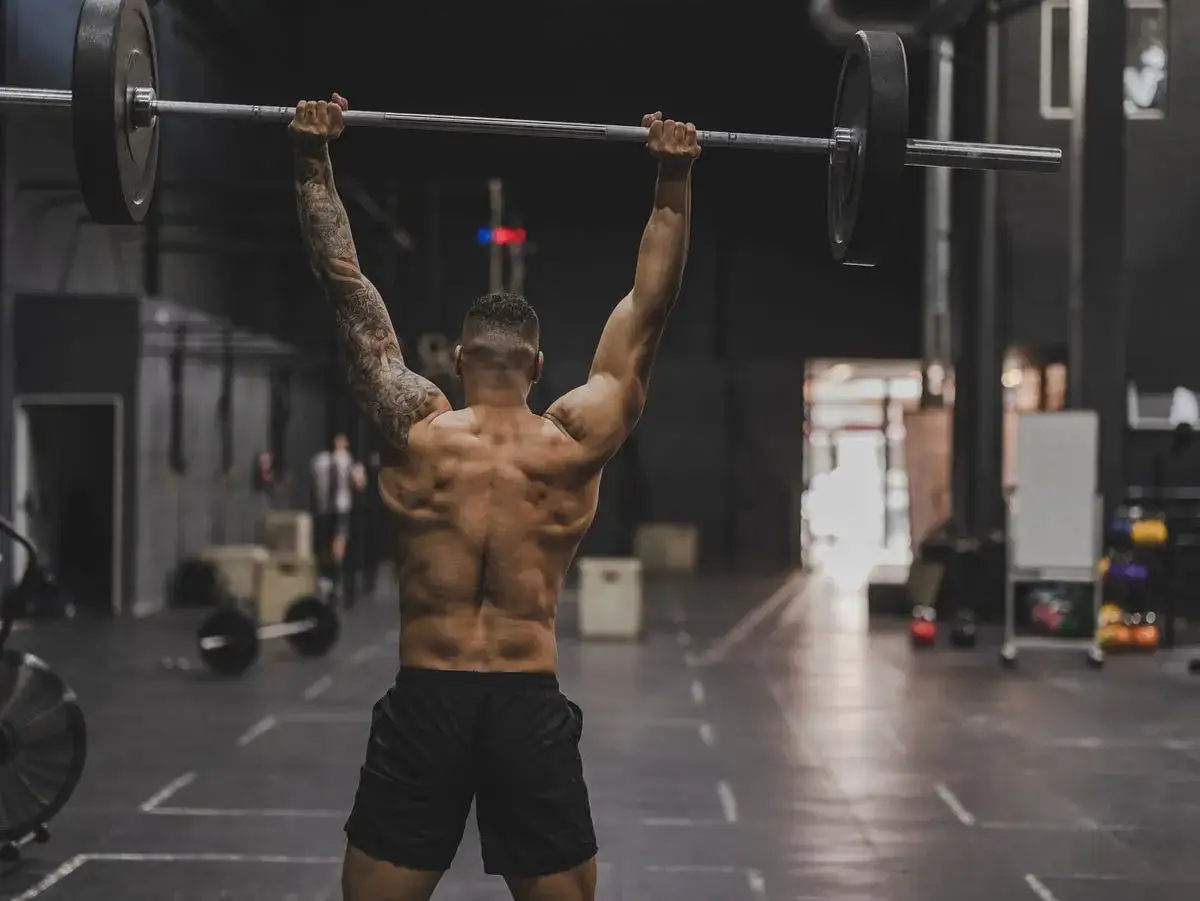 Ein Mann hebt eine Langhantel über dem Kopf. Dies ist ein Beispiel dafür, was hilft beim Muskelaufbau: Krafttraining im Fitnessstudio.