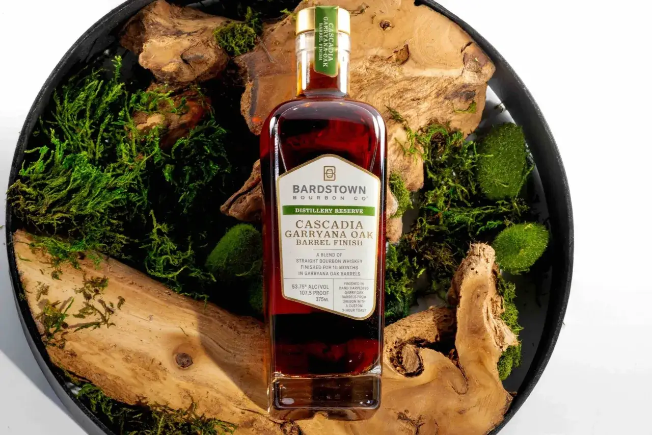Butelka bourbonu Cascadia Garryana Oak Barrel Finish od Bardstown Bourbon Co. w otoczeniu mchu i drewna. To jest bourbon co to jest.