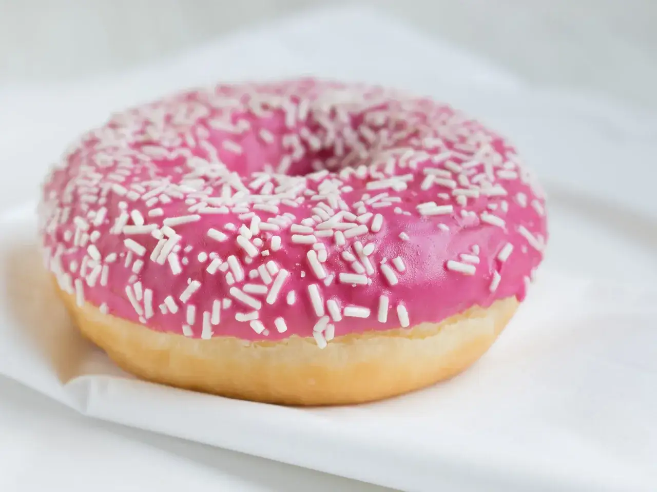 Ein leckerer Donut mit pinker Glasur und weißen Streuseln, bereit zum Genießen.
