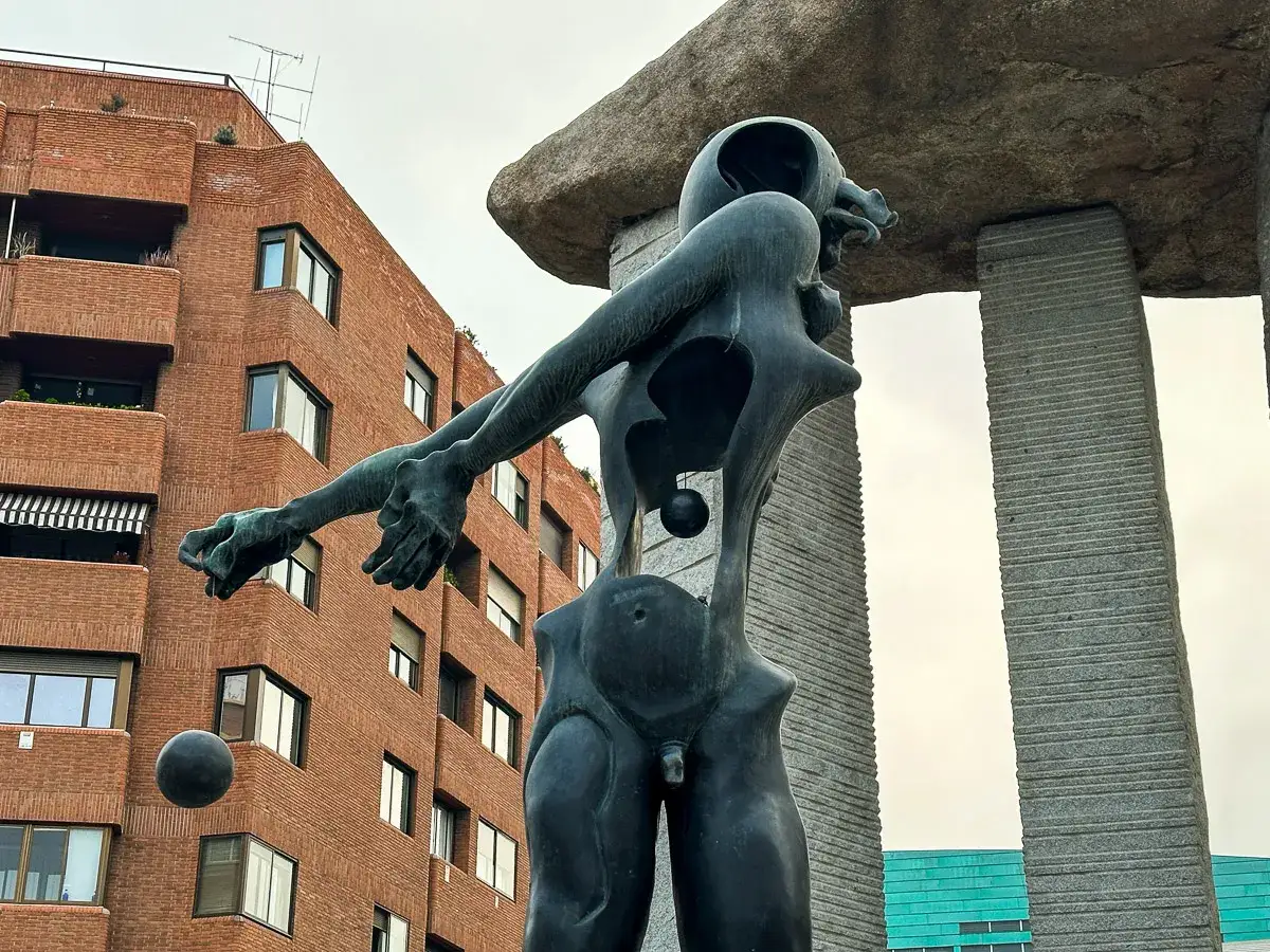 Madryt nietypowe atrakcje: surrealistyczny pomnik z kulami i ceglanym budynkiem w tle.