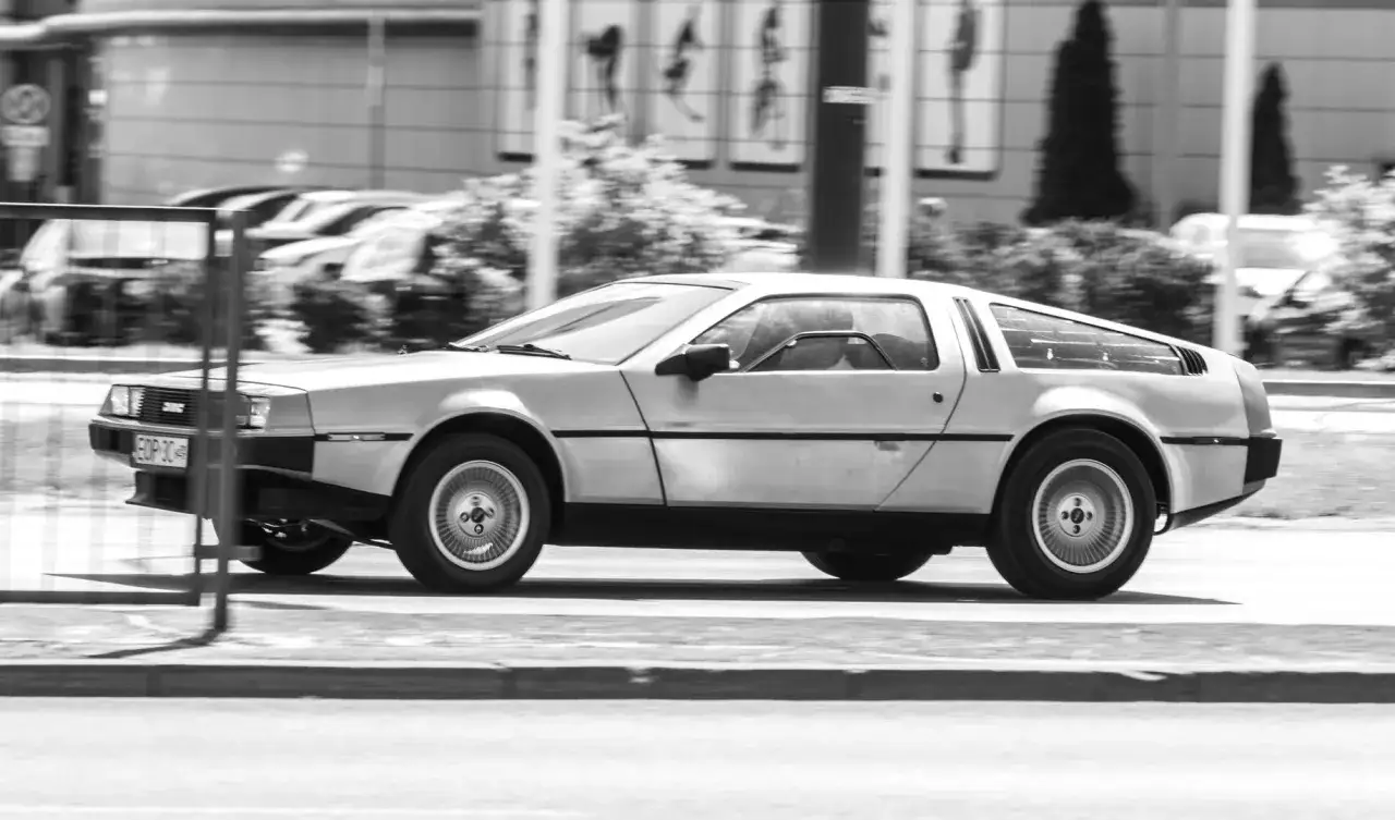 Srebrny DeLorean DMC-12 z tablicą rejestracyjną EOP 3C jedzie ulicą.