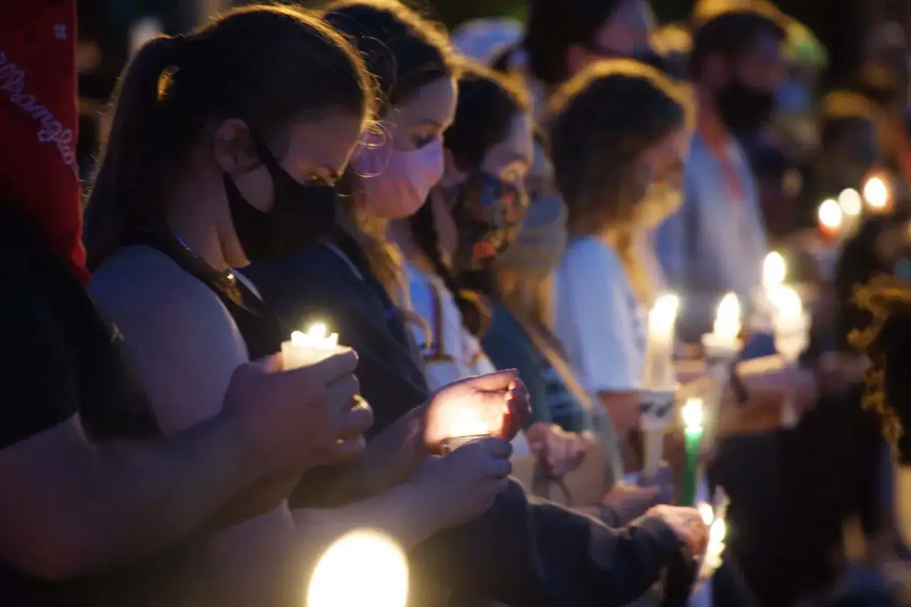 People hold candles at a vigil, their faces illuminated by the soft glow. The duration of vigils can vary, but this moment captures a shared sense of remembrance.