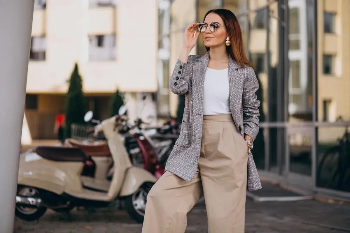 Rebecca Donaldson, con gafas de sol y un traje a cuadros, posa junto a una Vespa.