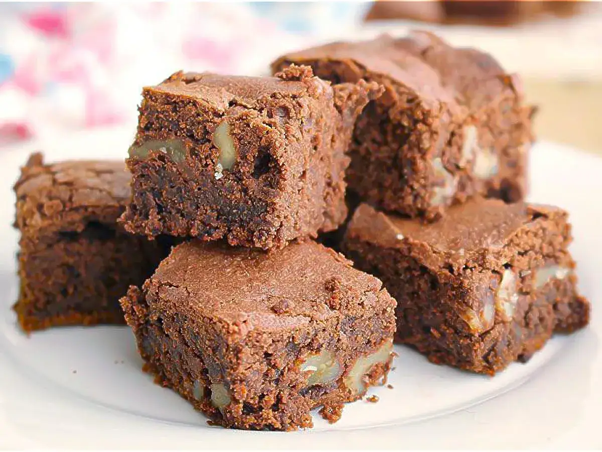Deliciosos trozos de brownie con nueces, apilados en un plato blanco.