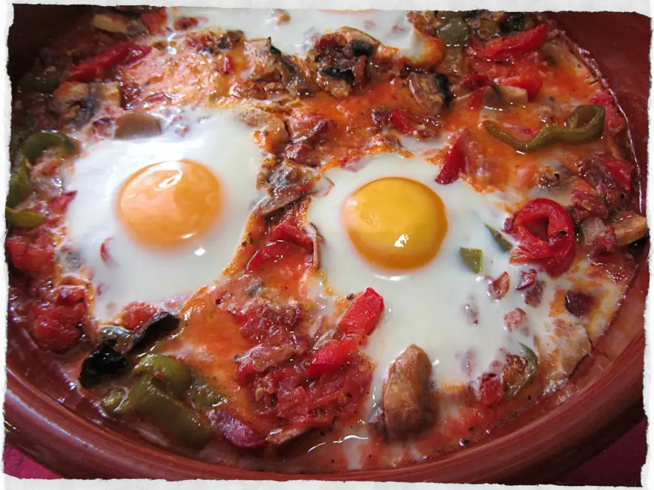 Dos huevos al plato con pimientos, tomate y champiñones en una cazuela de barro. ¡Un desayuno o cena delicioso!
