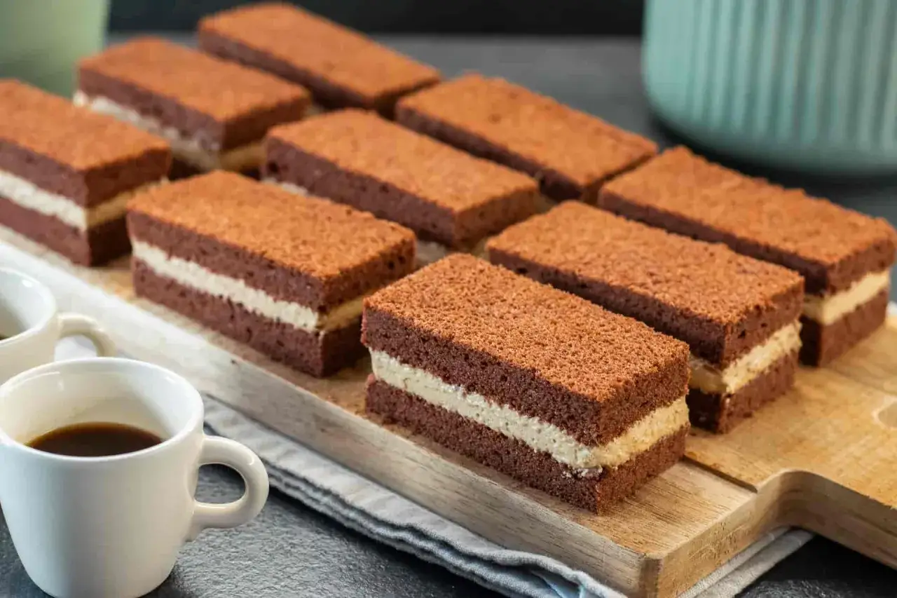 Deliziosi rettangoli di cheesecake al caff&egrave;, con strati di soffice pan di Spagna al cacao e crema chiara, pronti per essere gustati.