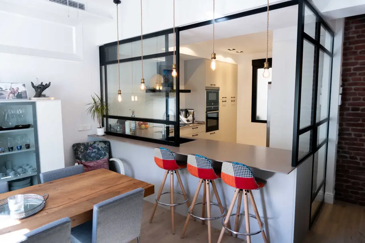 Cocina semiabierta al sal&oacute;n con barra de desayuno, taburetes coloridos y mesa de madera.
