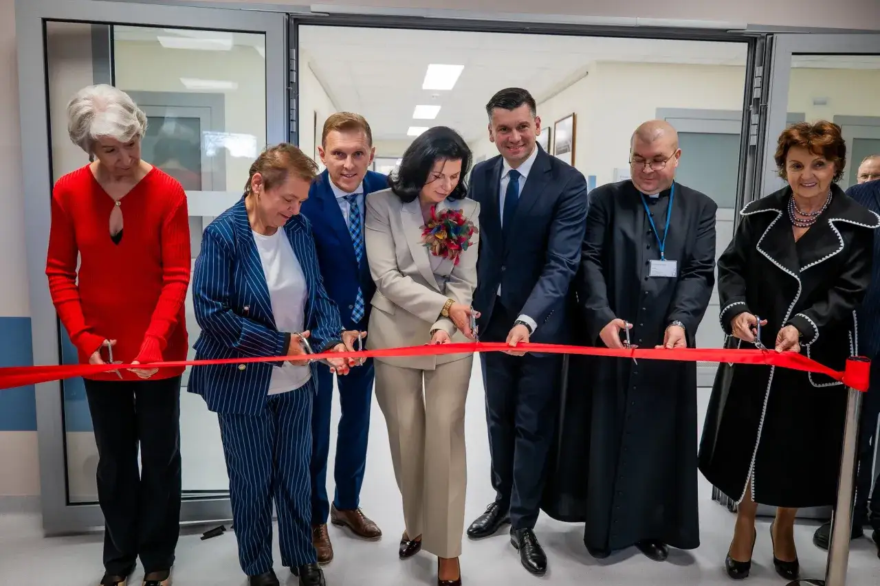 Uroczyste przecięcie czerwonej wstęgi przez grupę osób wewnątrz nowoczesnego budynku.