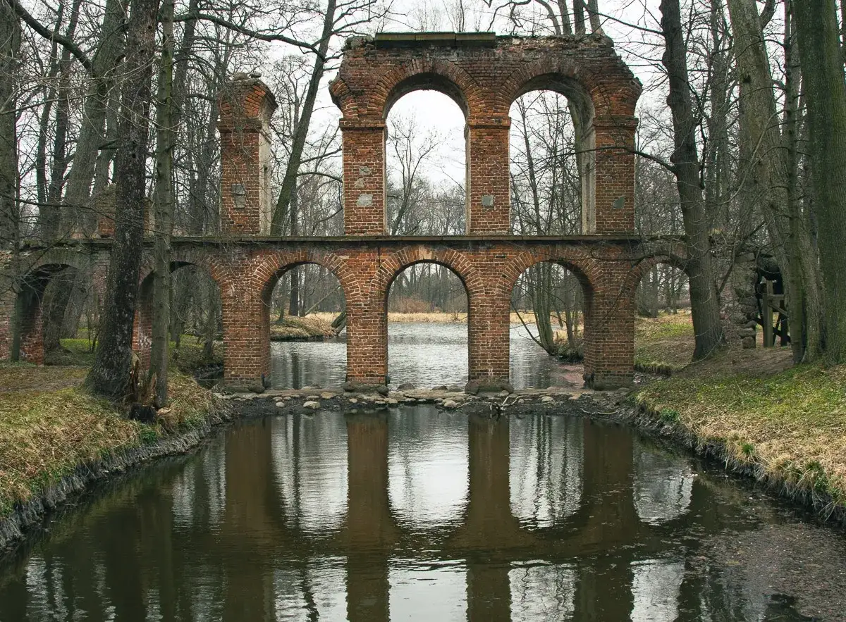 Ruiny pałacu w Nieborowie z ceglanymi arkadami nad wodą, otoczone drzewami.