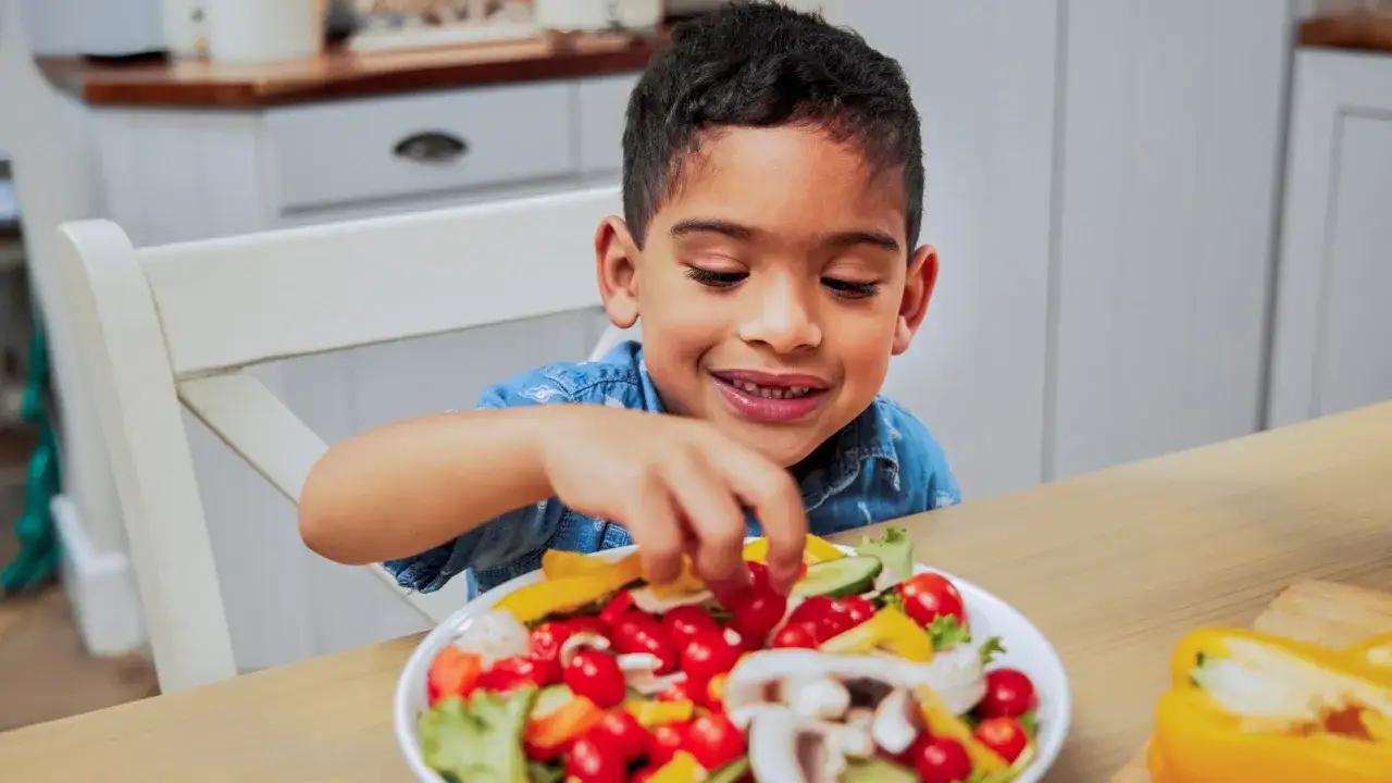 Niño sonriente elige tomates de una ensalada colorida, un paso clave para subir defensas niños.