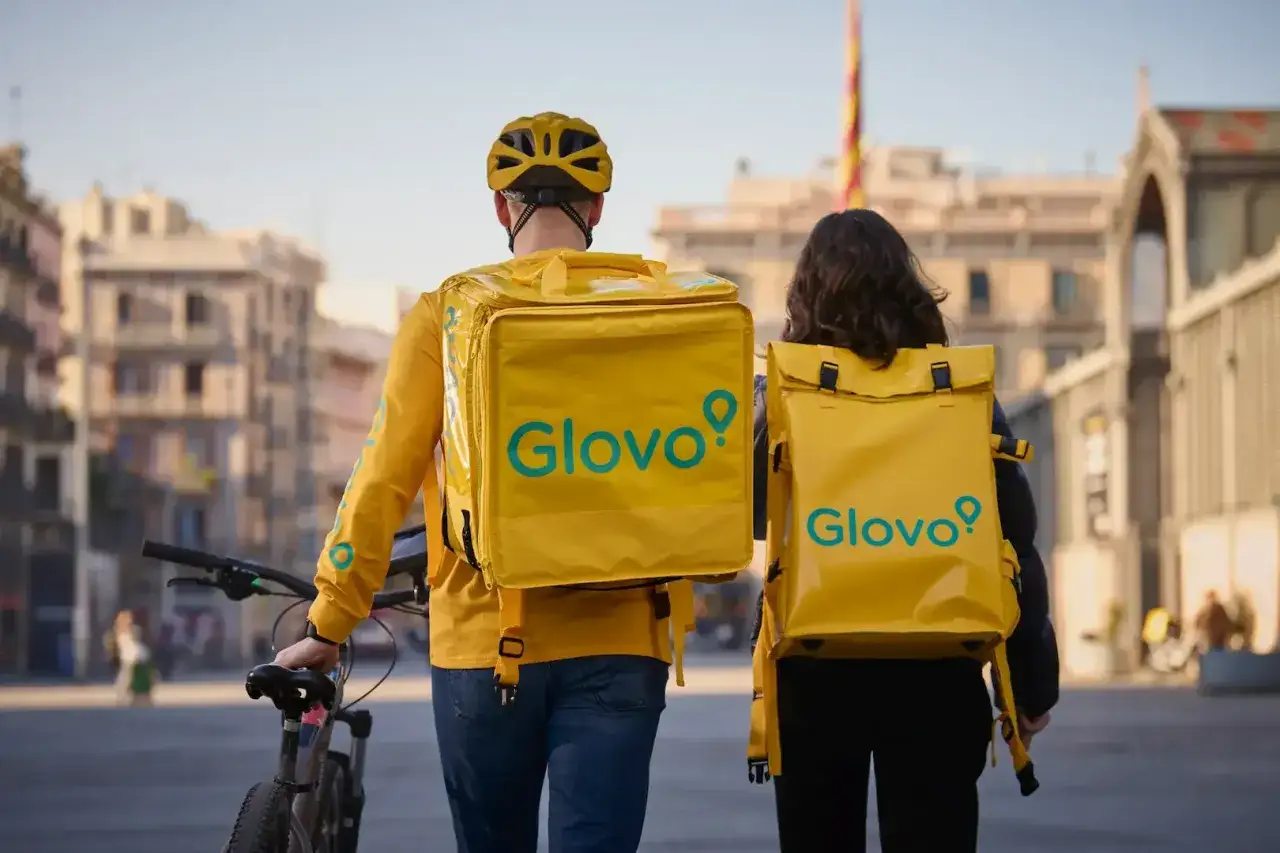 Dwie osoby z ż&oacute;łtymi plecakami Glovo idą ulicą. To świetna **glovo praca** dla każdego, kto lubi ruch i kontakt z ludźmi.