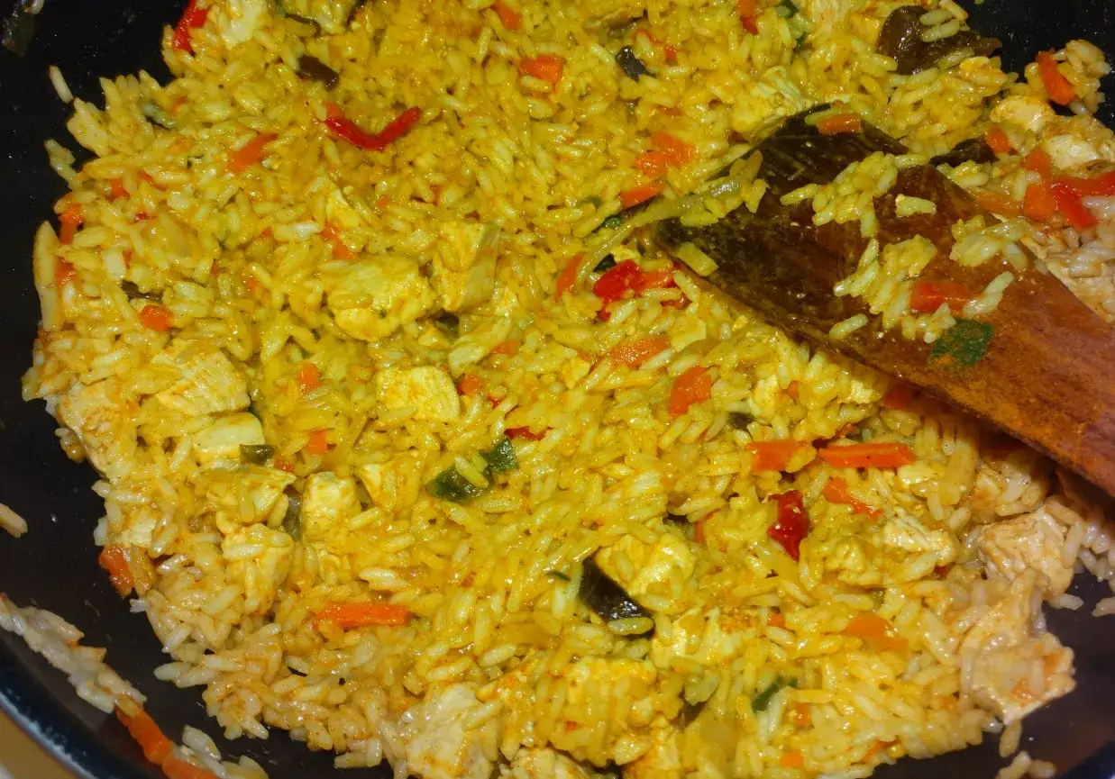Aromatyczny kurczak curry z ryżem i warzywami, mieszany drewnianą łyżką.