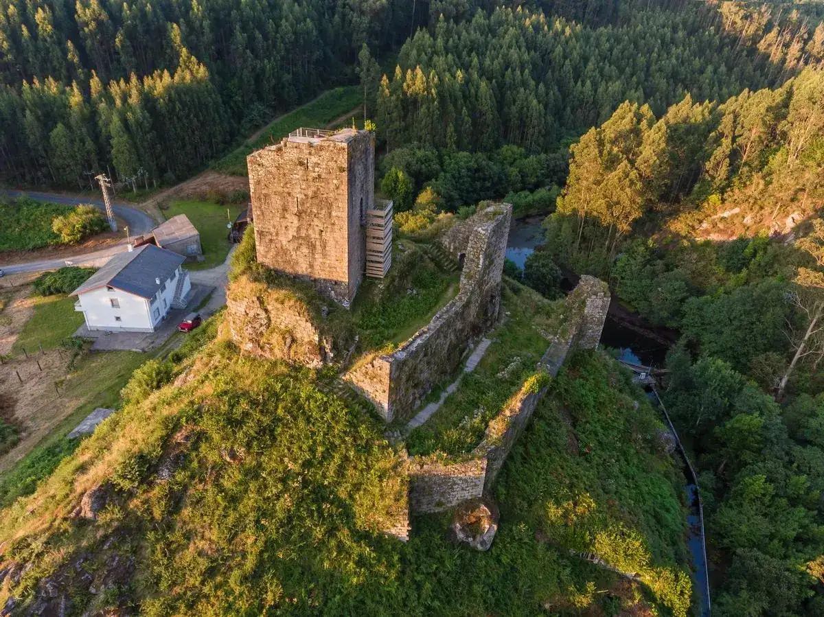 Las **torres de Altamira**, vestigios de un castillo medieval, se alzan sobre una colina verde, rodeadas de un bosque frondoso y un río.