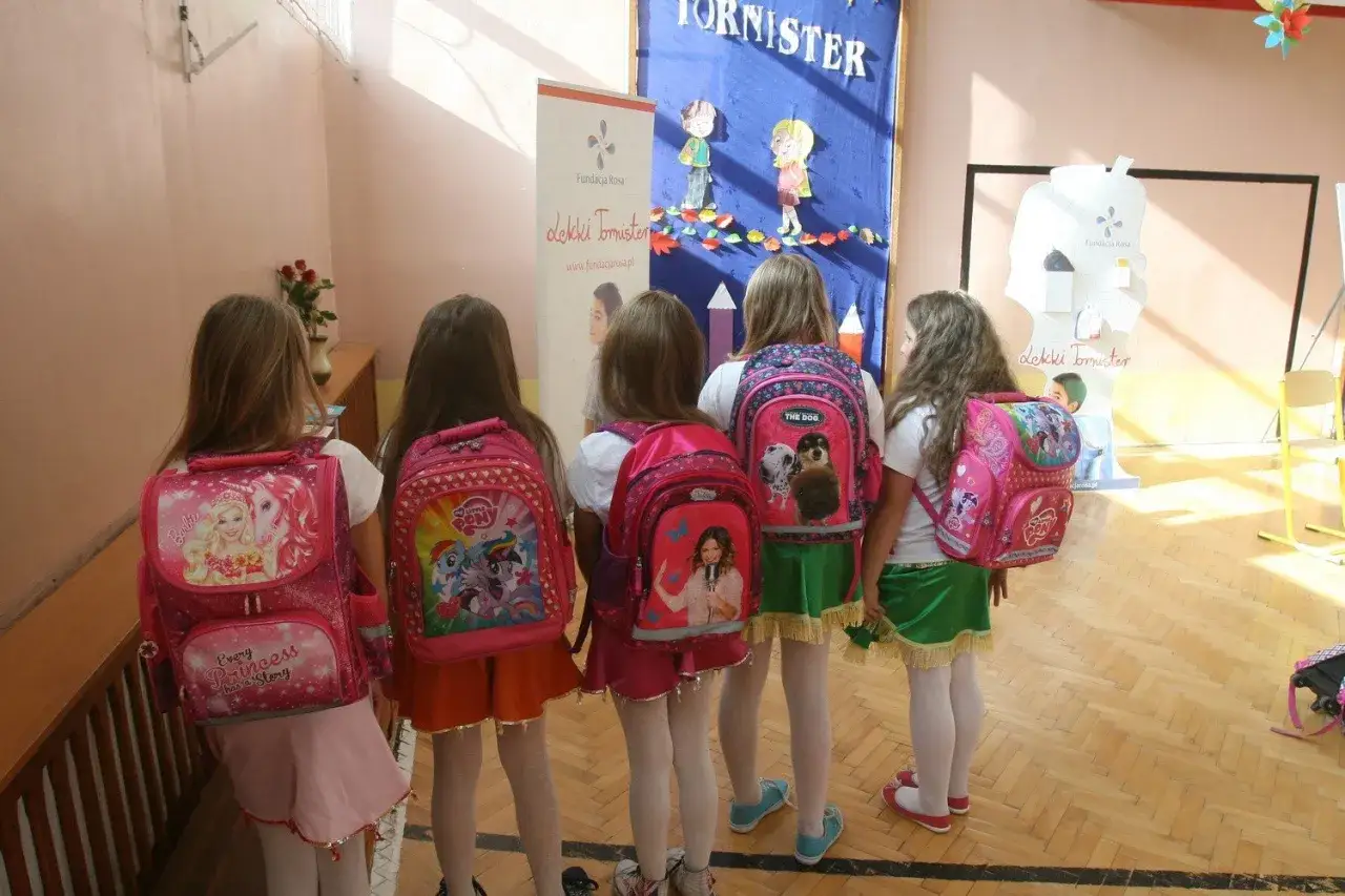 Dziewczynki w pierwszych klasach szkoły podstawowej, gotowe na nowy rok szkolny, z plecakami ozdobionymi postaciami z bajek.