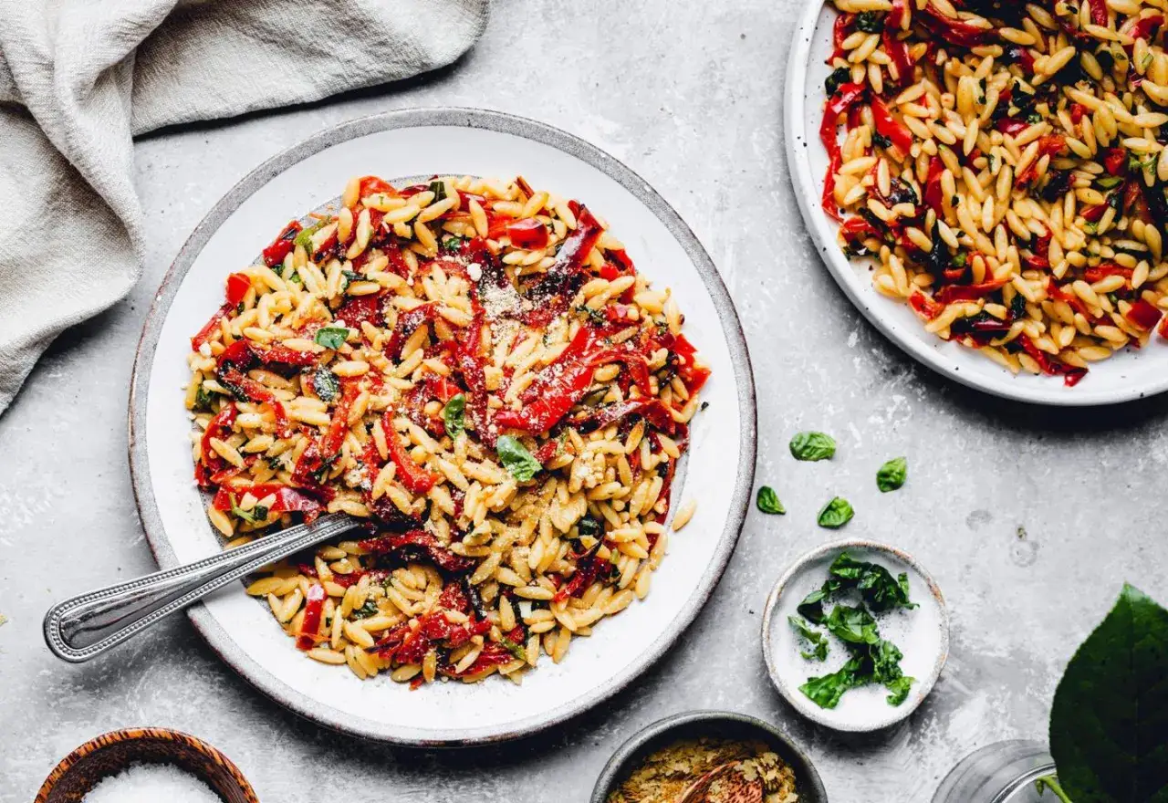 Teller mit griechischen Nudeln, roten Paprika und Basilikum. Ein L&ouml;ffel liegt im Essen.