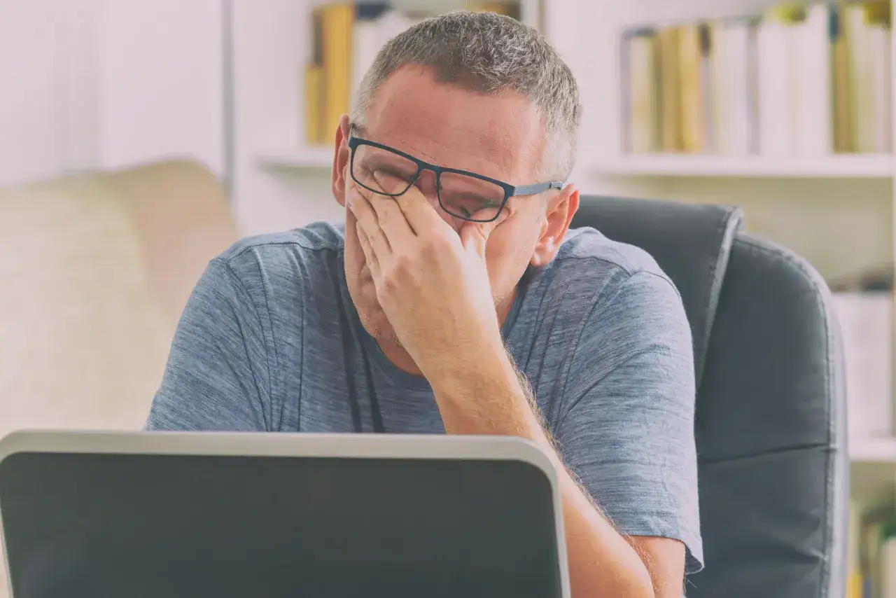 Hombre con gafas se frota los ojos, agotado frente a su port&aacute;til. Busca c&oacute;mo quitar la fatiga.