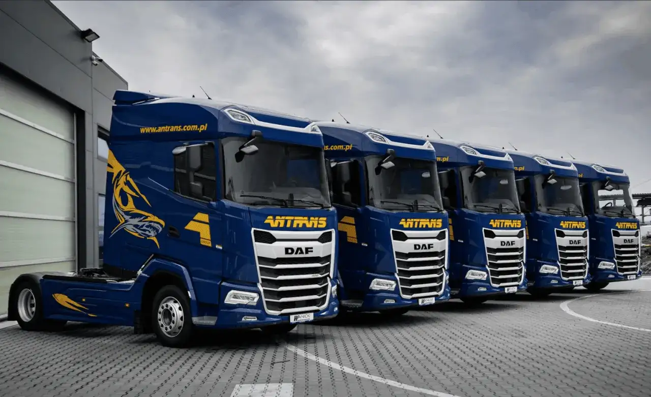 Rząd niebieskich tirów DAF z logo Antrans i grafiką rekina. Gotowe do trasy.