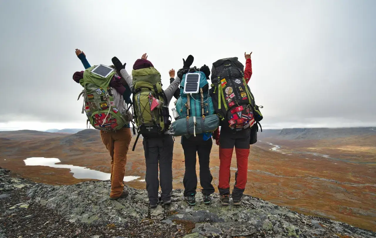 Vier Wanderer mit vollgepackten Rucksäcken für eine Mehrtagestour stehen auf einem Felsen und blicken in eine weite Landschaft.