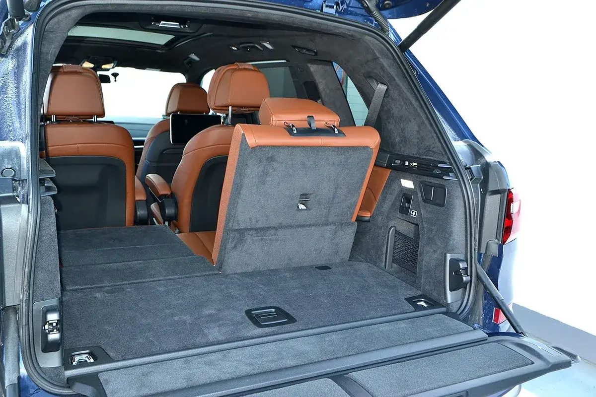 Wnętrze luksusowego SUV-a z brązową skórzaną tapicerką. Tylne siedzenia złożone, tworząc płaską przestrzeń bagażową. Idealne na rodzinne wycieczki x7.