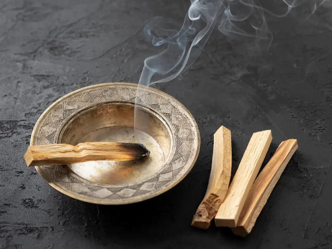 Un palo santo arde en un cuenco de metal, liberando humo. A su lado, tres palos de palo santo sin quemar. &iquest;Por qu&eacute; se apaga el palo santo?
