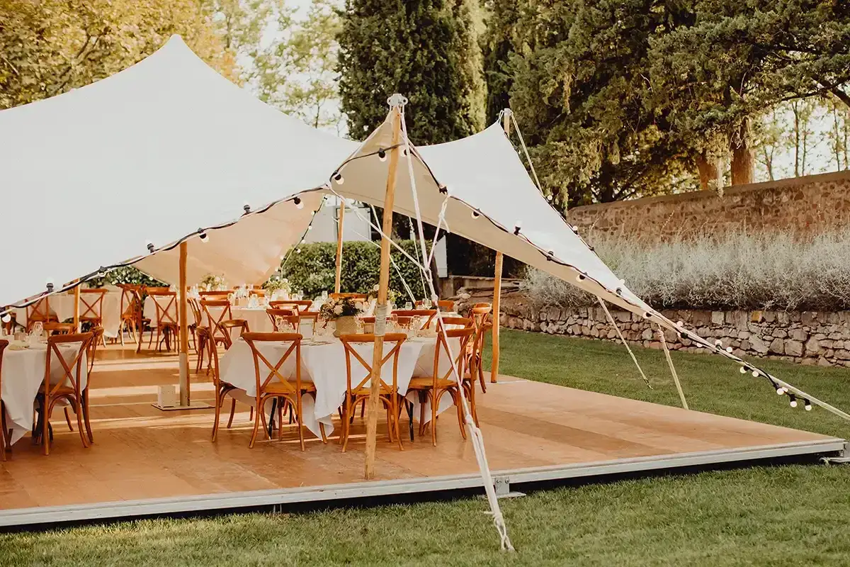 Festlich gedeckte Tische unter einem weißen Zelt, bereit für eine Hochzeit. Lichterketten spannen sich über das Dach, als Schutz vor möglichem Hochzeit Regen.