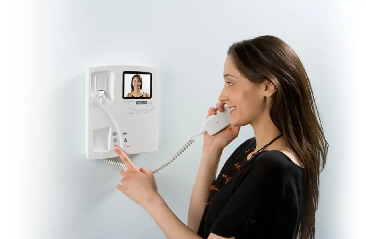 Mujer sonríe mientras usa un citófono en España. La pantalla muestra a otra mujer.