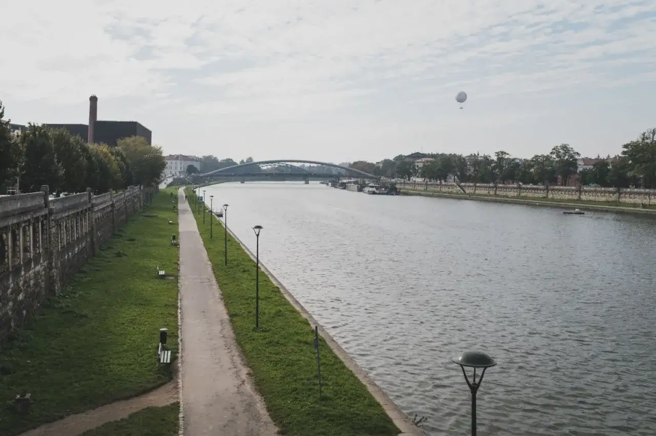 Spacer po bulwarach nad Wisłą, rzeką, nad którą leży Kraków. W oddali widać most i balon.