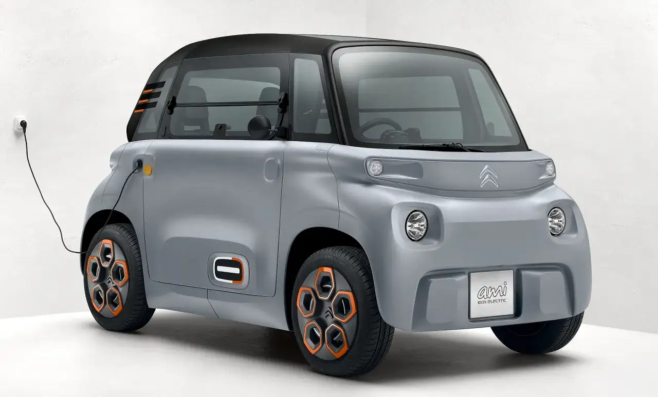 Szary Citroen Ami 100% Electric, podłączony do ładowania, z pomarańczowymi akcentami na felgach i karoserii.