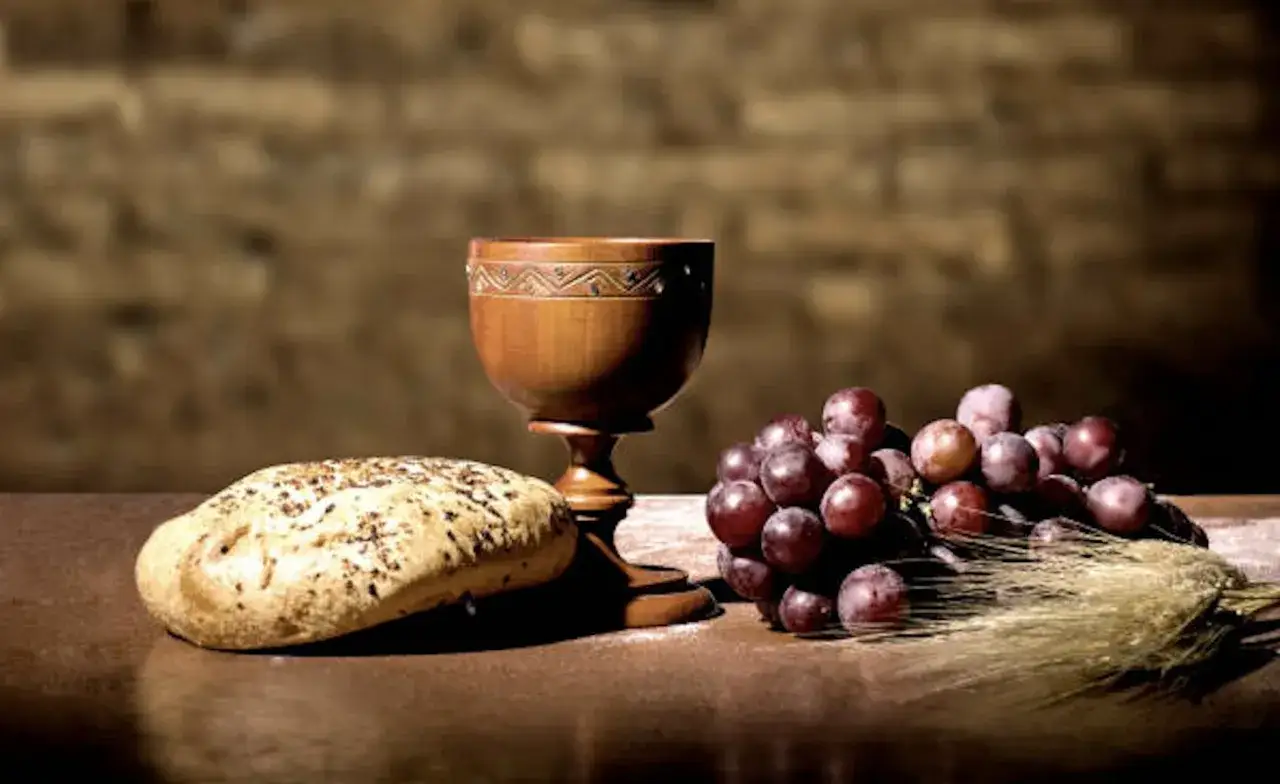 A wooden chalice, bread, and grapes sit on a table, evoking the simplicity of a monk diet.