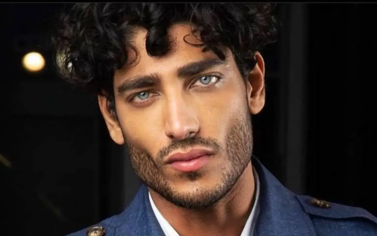Primo piano di un uomo con splendidi capelli ricci uomo e occhi azzurri penetranti, indossa una giacca blu scuro.