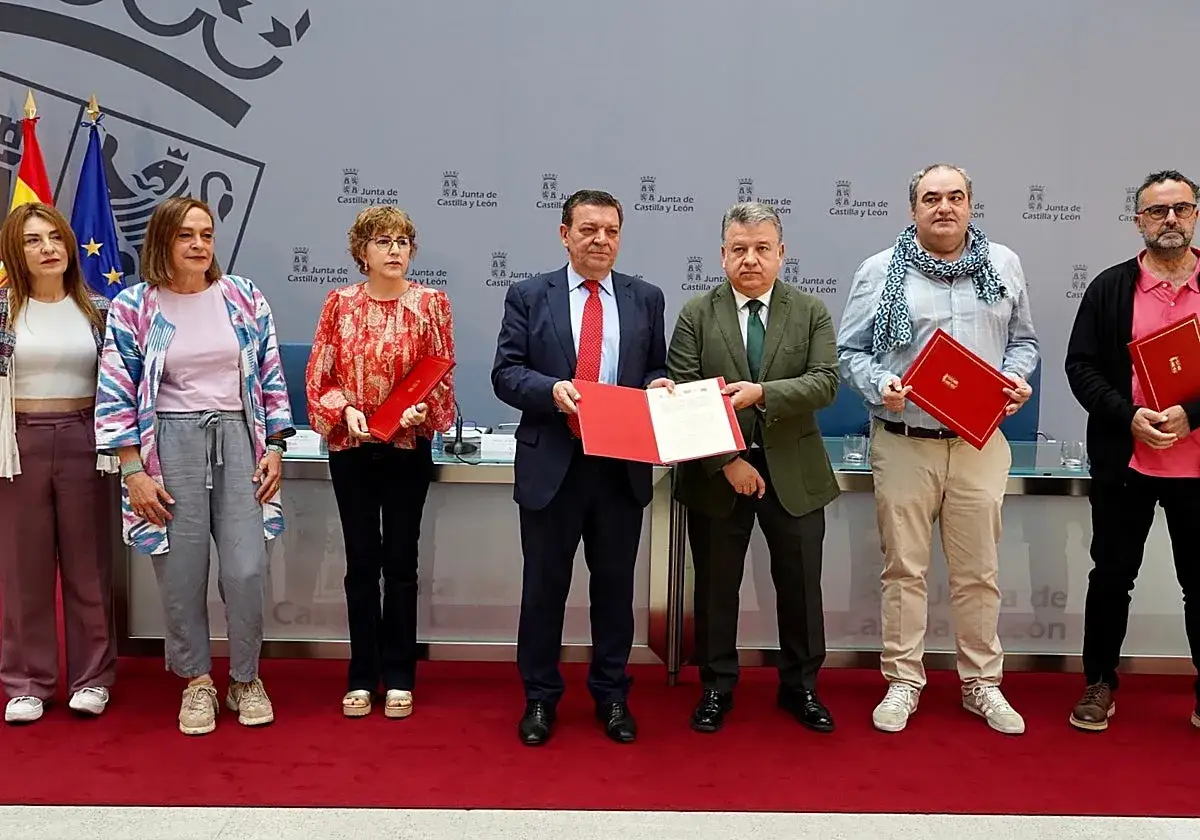 Grupo de personas posando con documentos, posiblemente un precontrato de trabajo, ante un fondo con el escudo de Castilla y Le&oacute;n.