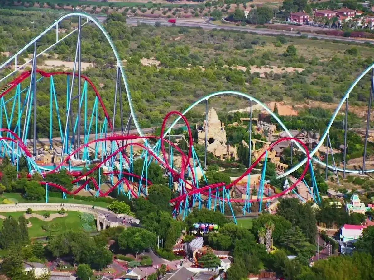Vista aérea de espectaculares parques de atracciones en España, con montañas rusas de colores vibrantes serpenteando entre la vegetación y edificios temáticos.