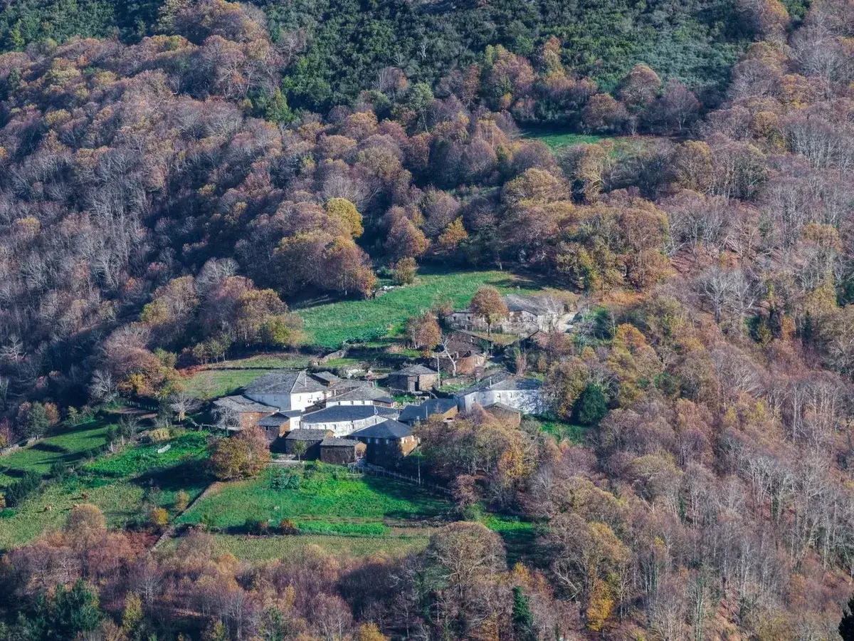 Pueblo de casas de piedra en la Serra do Courel, rodeado de bosques otoñales y prados verdes.