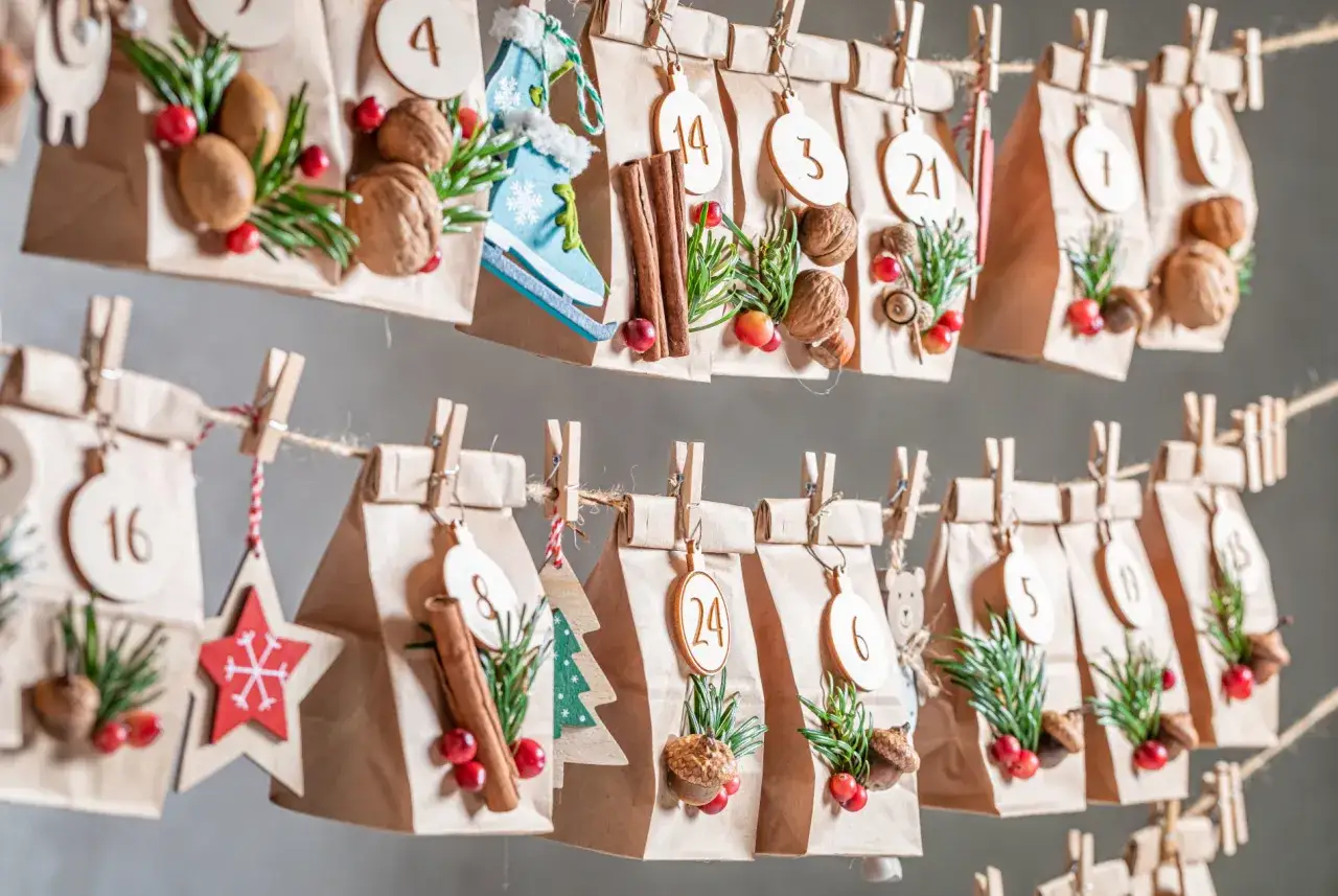 Bolsitas de papel kraft decoradas con piñas, bayas y números, colgadas como un calendario de adviento. ¡Una idea genial para saber como hacer calendario de adviento!