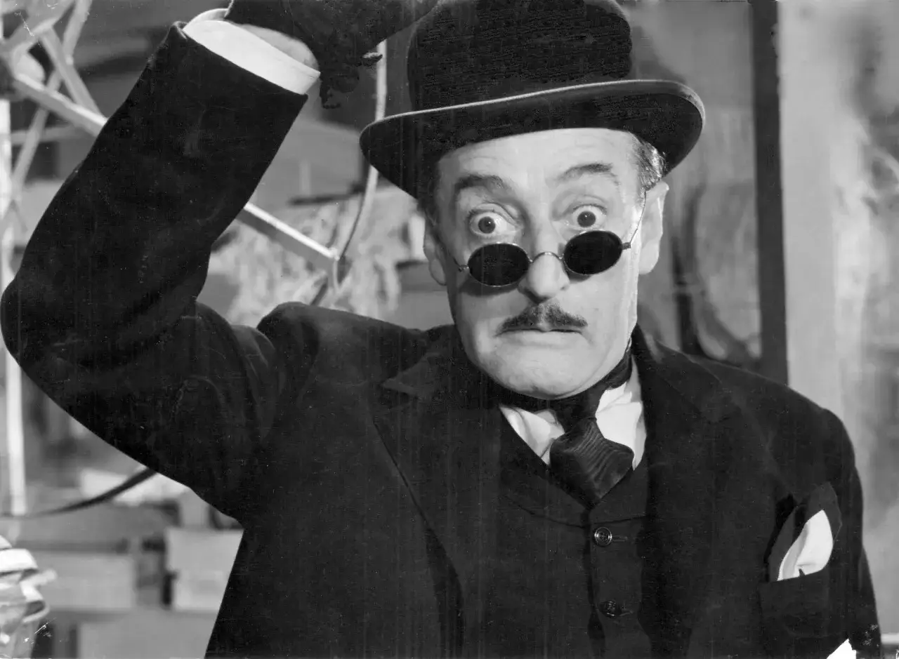 Un attore napoletano con un cappello e occhiali tondi, espressione sorpresa.