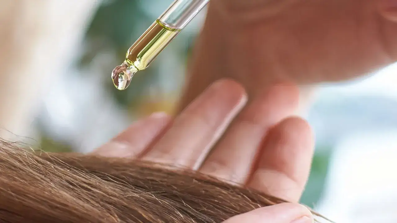 Kropla olejku na pipetce nawilża suche końcówki włosów.