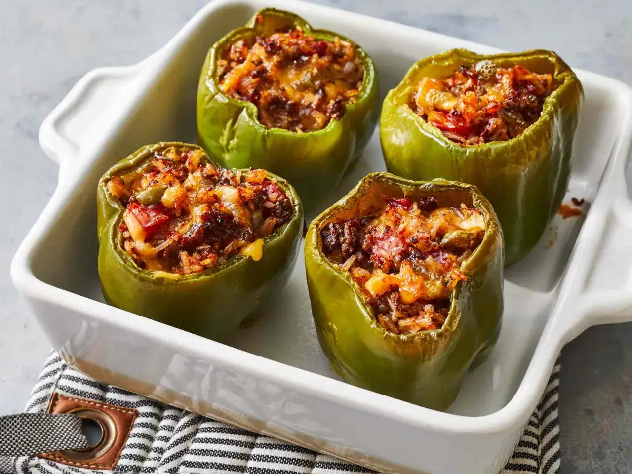 Quatre poivrons verts garnis d'un mélange savoureux de viande, de riz et de fromage, prêts à être dégustés. Ces légumes farcis sont un délice.