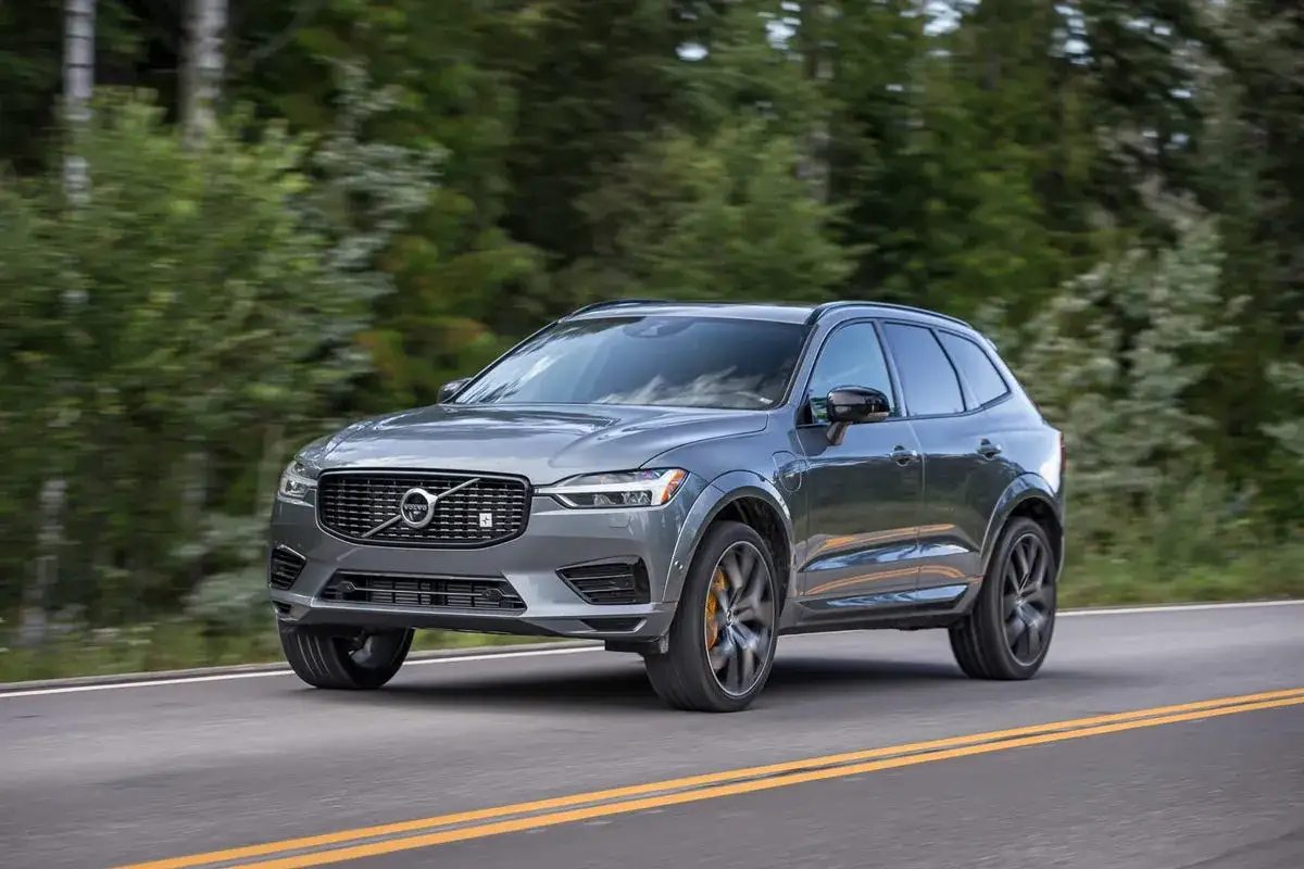 Szary Volvo XC60 Polestar mknie po asfaltowej drodze wśród zielonych drzew.
