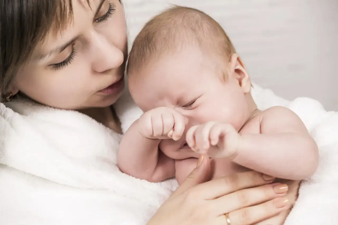 Madre reconforta a su beb&eacute;, que parece tener una crisis de 8 meses, acurrucados en una manta blanca.