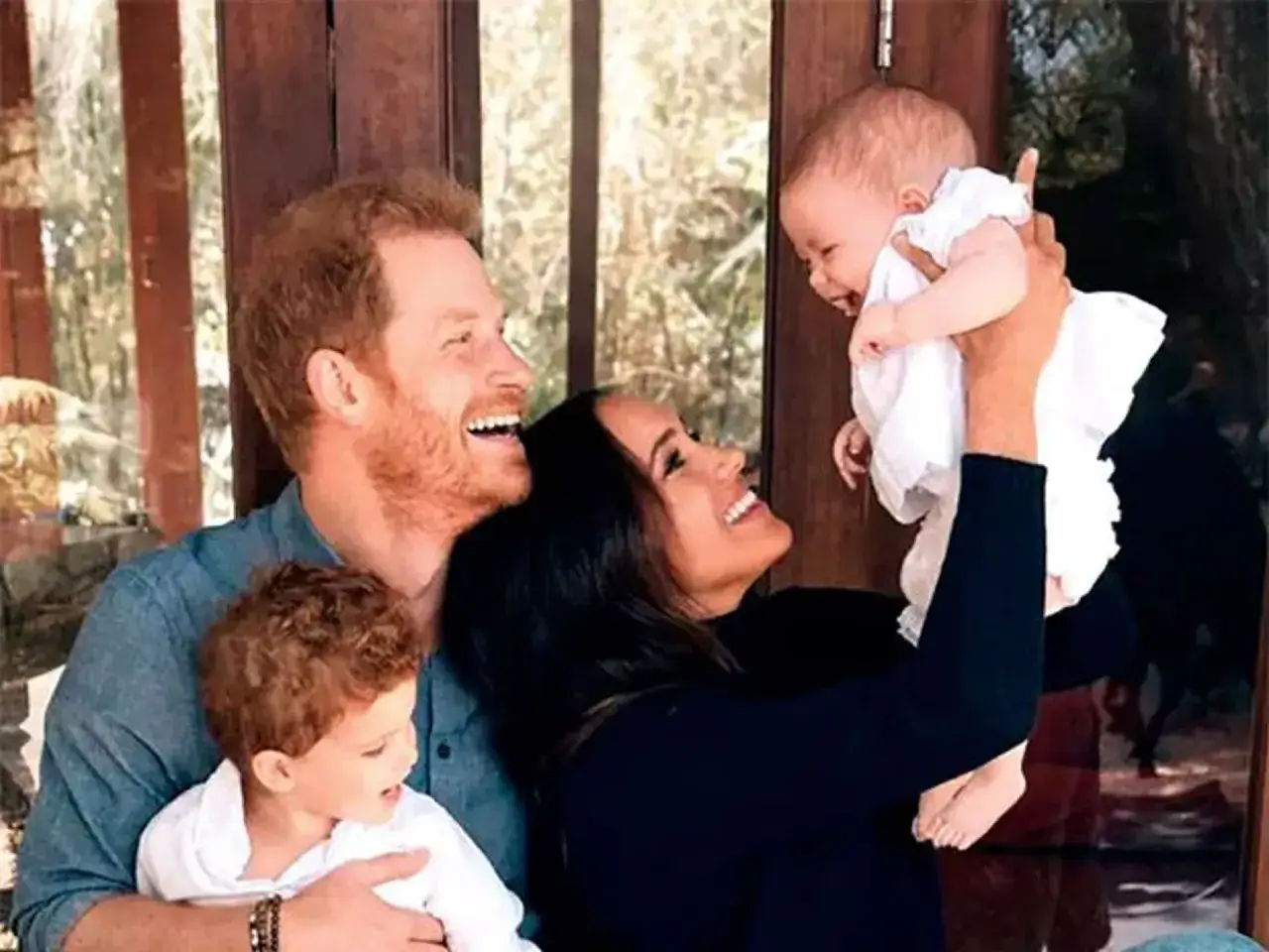Meghan Markle y el Príncipe Harry sonríen mientras sostienen a sus hijos, un niño pequeño y un bebé, en un momento familiar tierno.