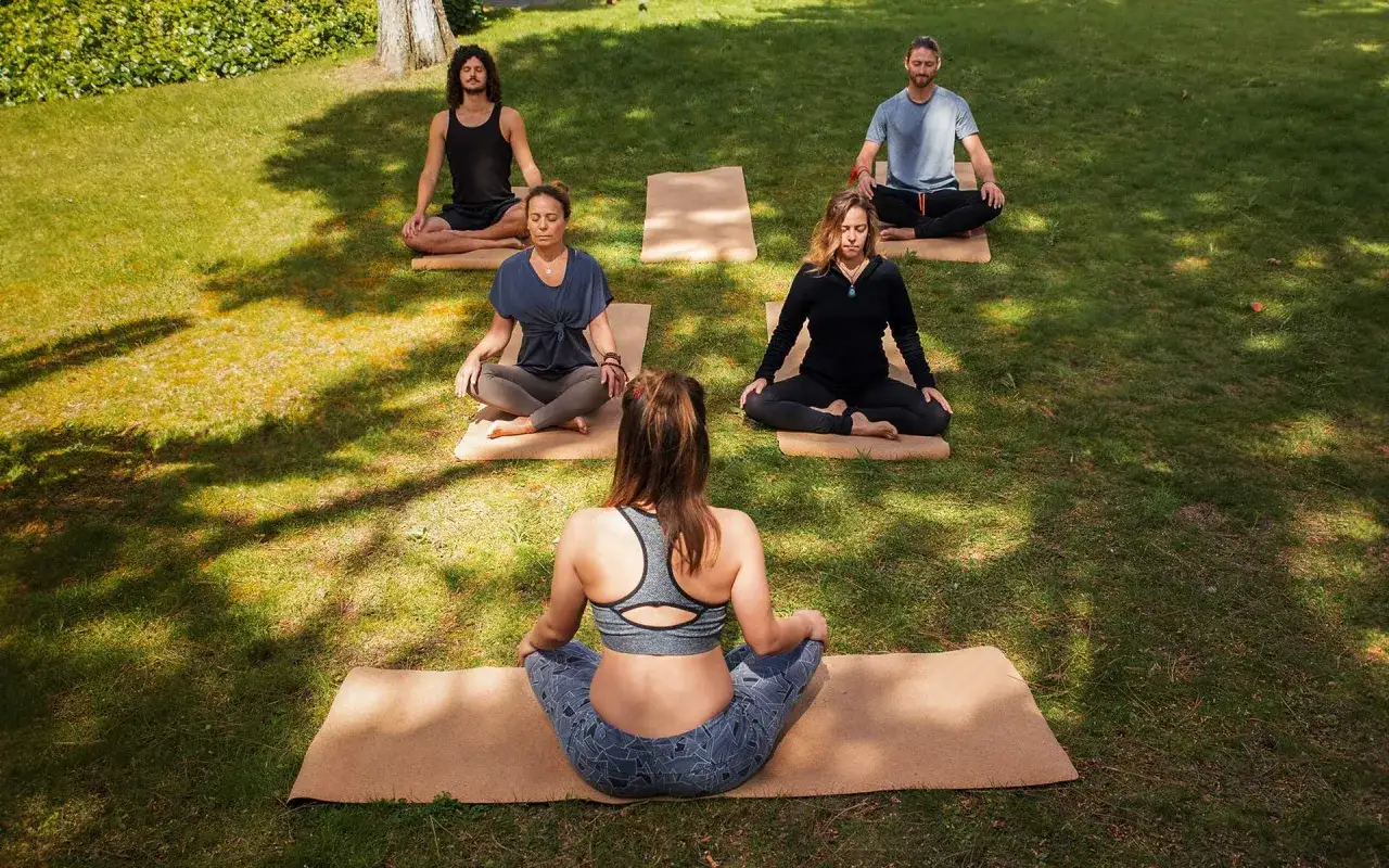 Fem personer mediterar utomhus på yogamattor i gräset. De sitter i lotusställning, en övning som kan hjälpa till att minska dukkha, lidande, inom buddhismen.