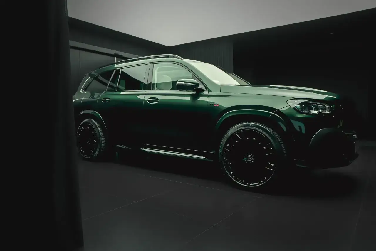 Zielony Mercedes Brabus z czarnymi felgami i detalami, prezentujący się w nowoczesnym wnętrzu.