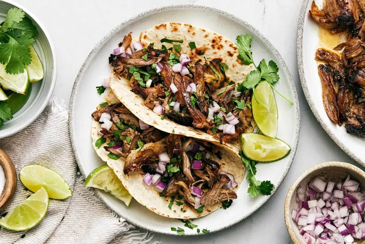 Tv&aring; carnitas-tacos med l&ouml;k och koriander, serverade med limeklyftor. Ett perfekt carnitas recept f&ouml;r en festm&aring;ltid.