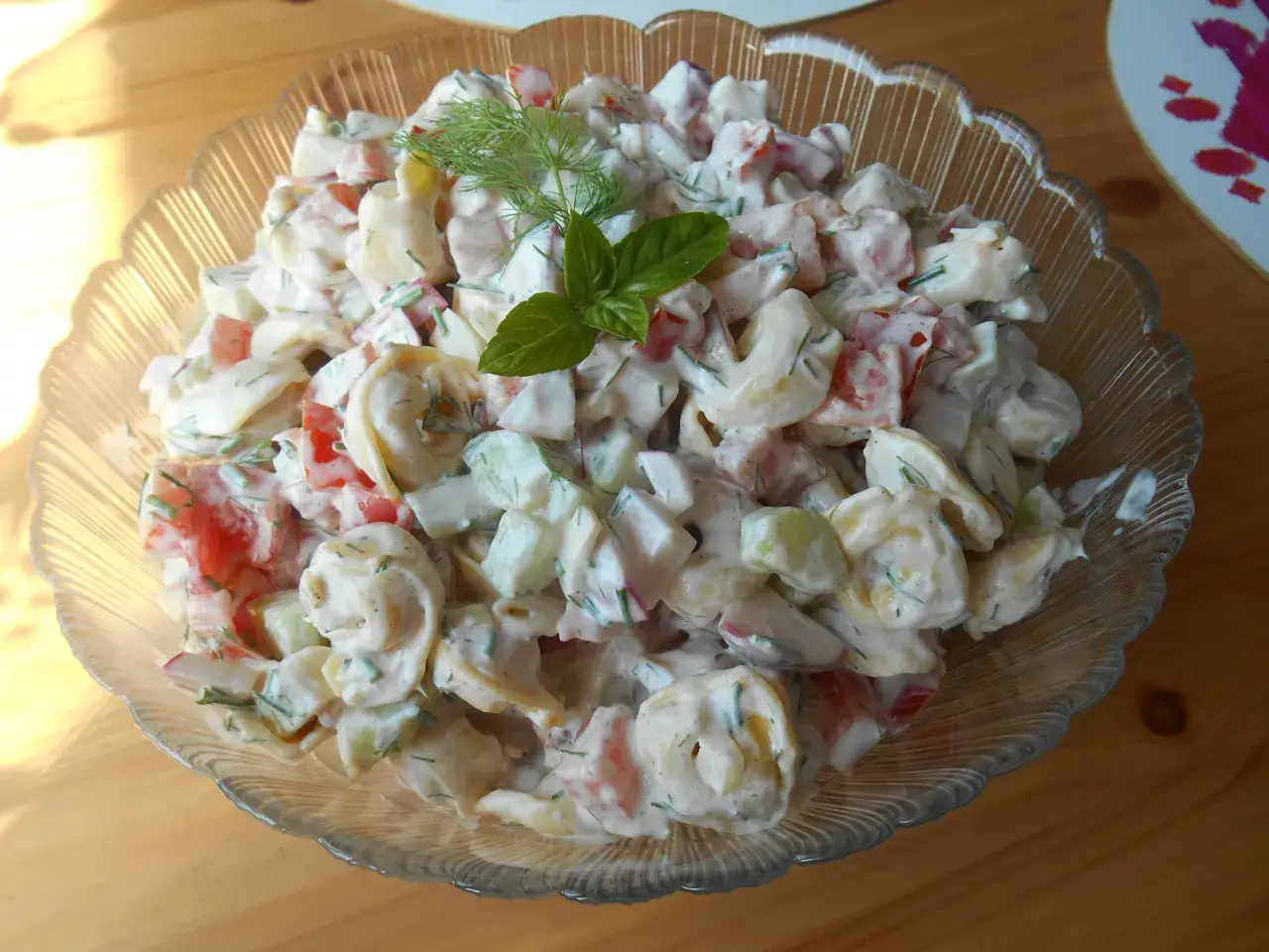 Pyszna, kremowa najlepsza sałatka z tortellini z pomidorami i ogórkiem, udekorowana bazylią i koperkiem.