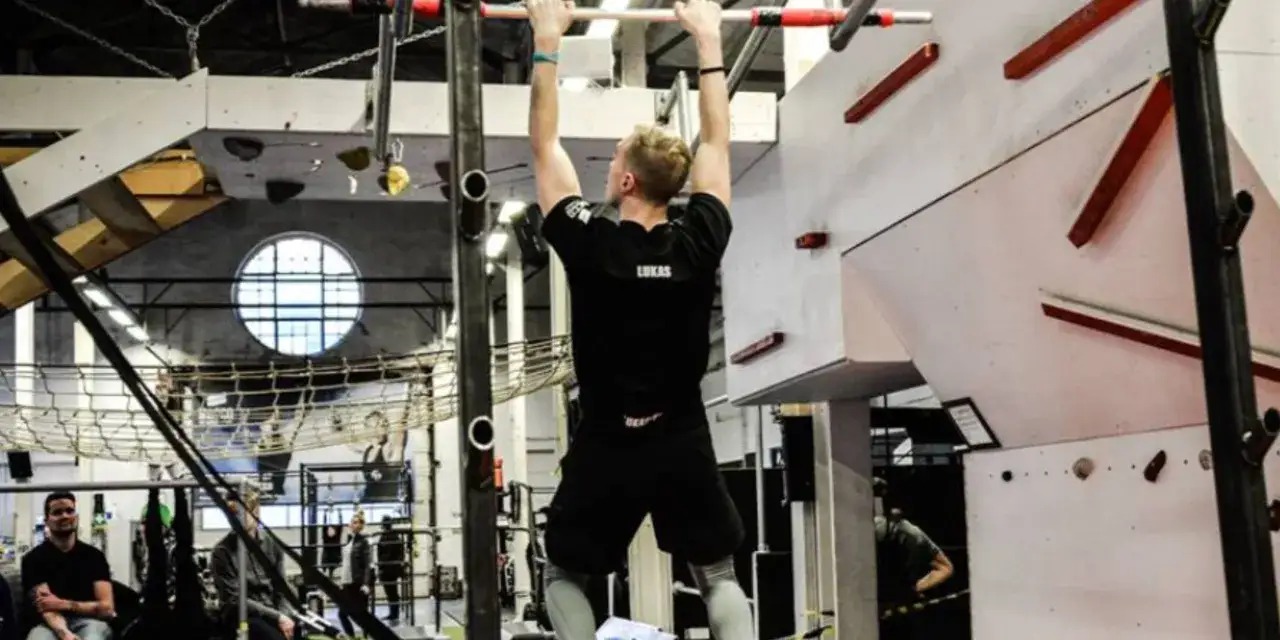Man tränar pull-ups i en hinderbana, en del av ocr sport.