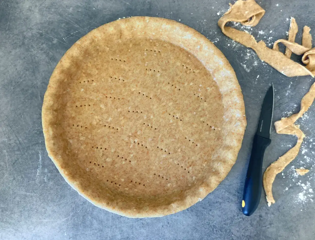En f&auml;rdigbakat pajskal med prickar, redo f&ouml;r fyllning. Bredvid ligger degrester och en kniv. Ett perfekt pajdeg recept!