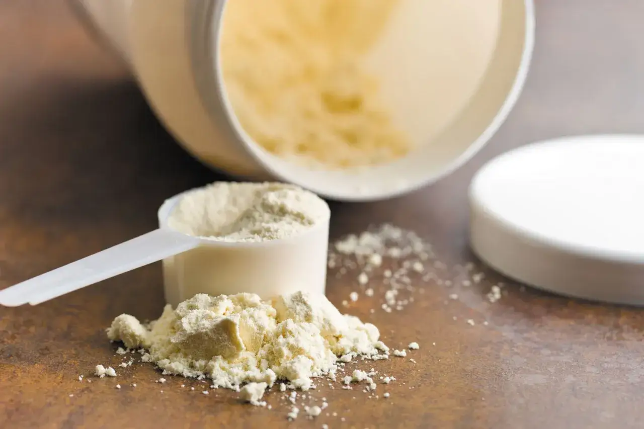 Ein Messl&ouml;ffel mit Proteinpulver, das aus einem umgekippten Beh&auml;lter rieselt. Die Frage, ob Proteinpulver krebserregend ist, besch&auml;ftigt viele.