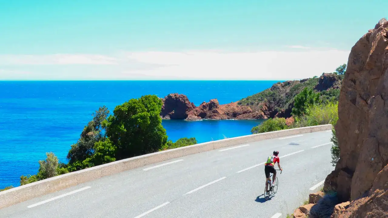 Radfahrer auf der Nizza Route genie&szlig;t die atemberaubende K&uuml;stenlandschaft mit t&uuml;rkisfarbenem Meer und roten Felsen.