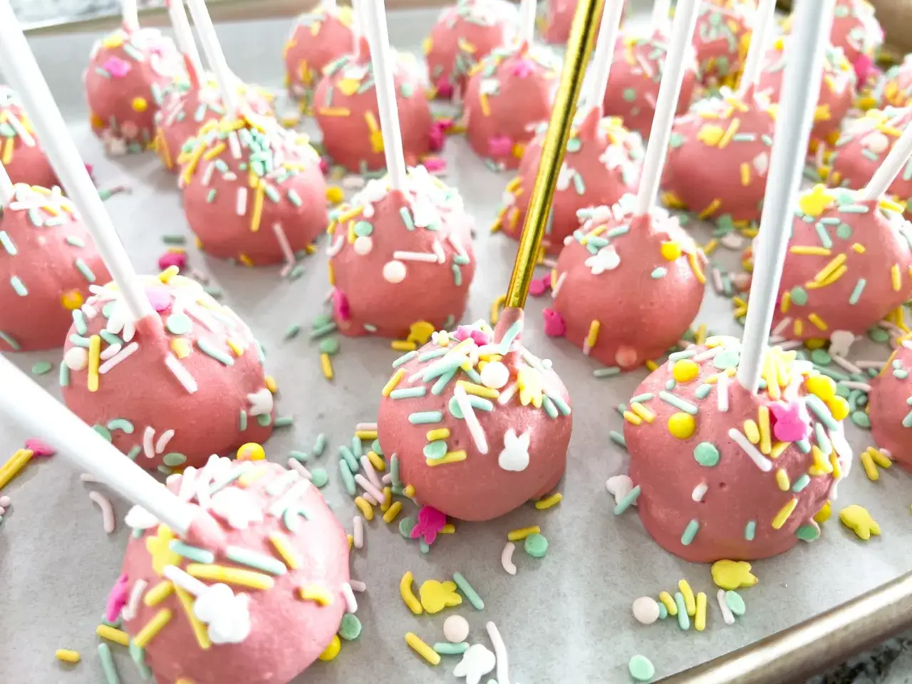 Różowe cake pops ozdobione kolorową posypką i króliczkami, gotowe na wielkanocne przyjęcie.